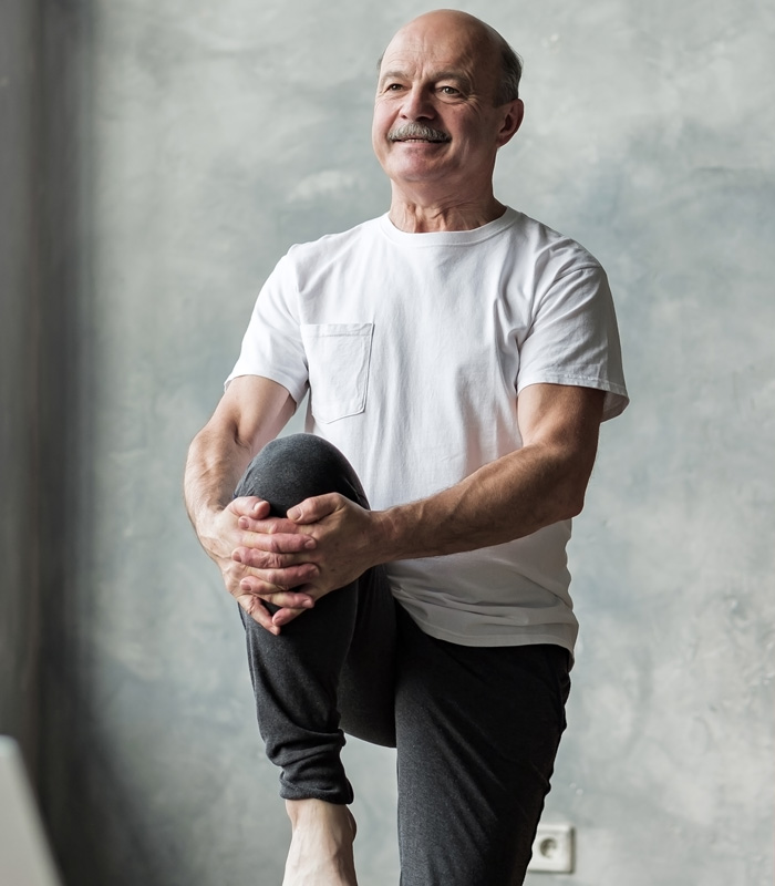 Smiling senior balancing as he lifts his right leg and holds his knee